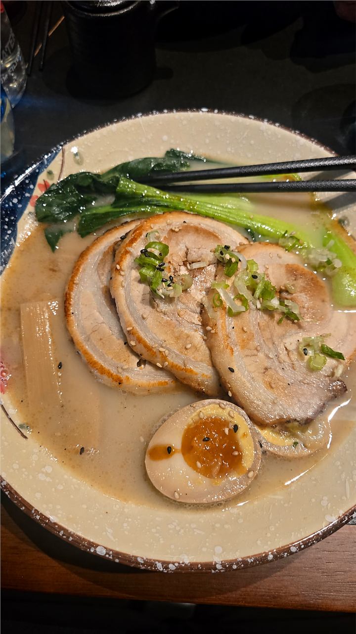 Eine Schale Ramen mit Schweinefleisch, Ei, grünem Gemüse und Essstäbchen